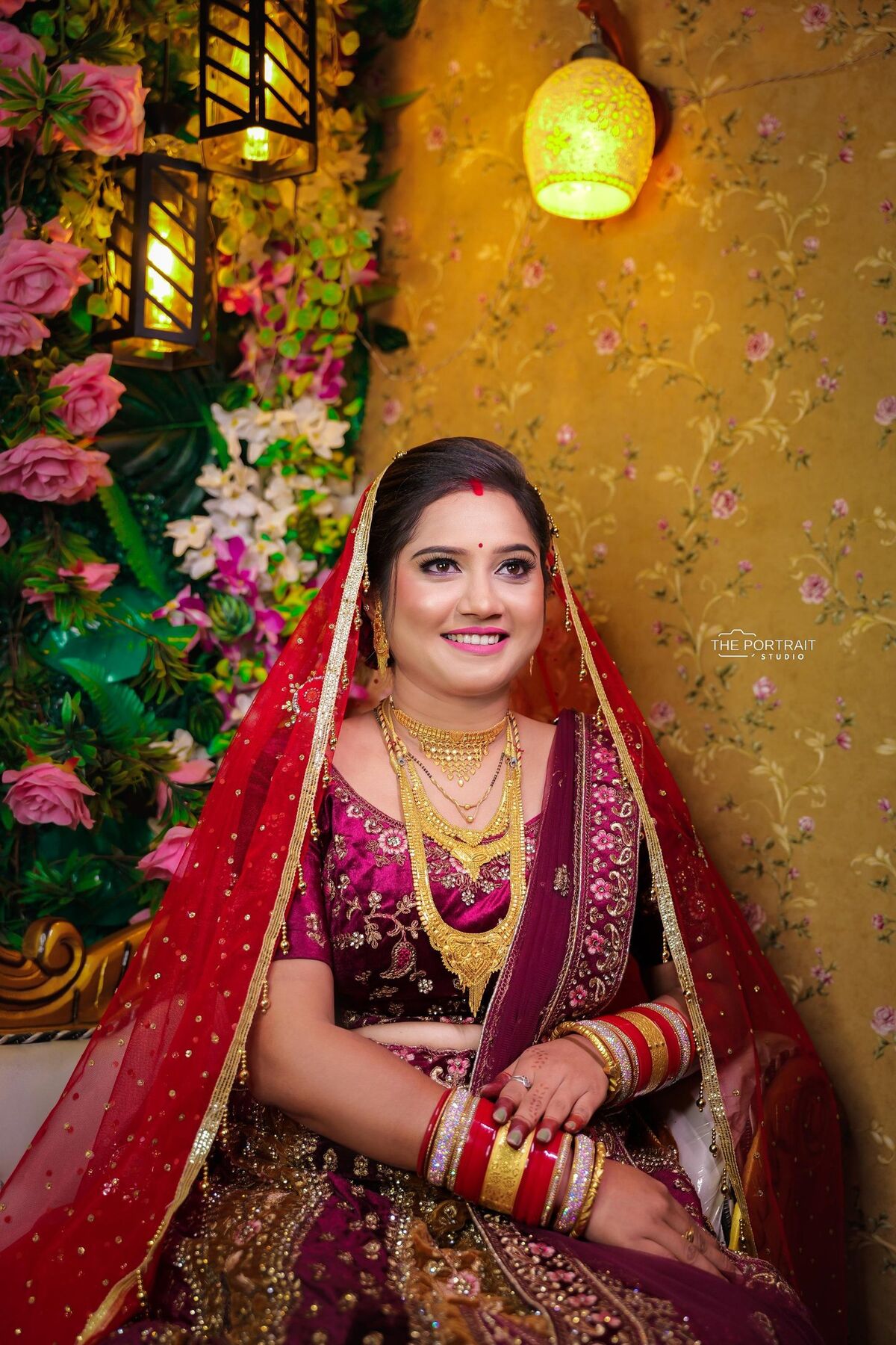 Bride in a red dupatta beside a floral wall and lanterns