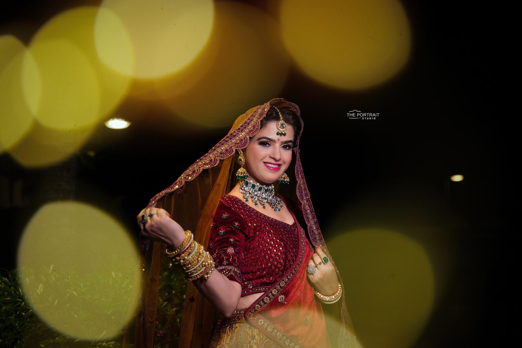 Bride in maroon lehenga against golden bokeh lights