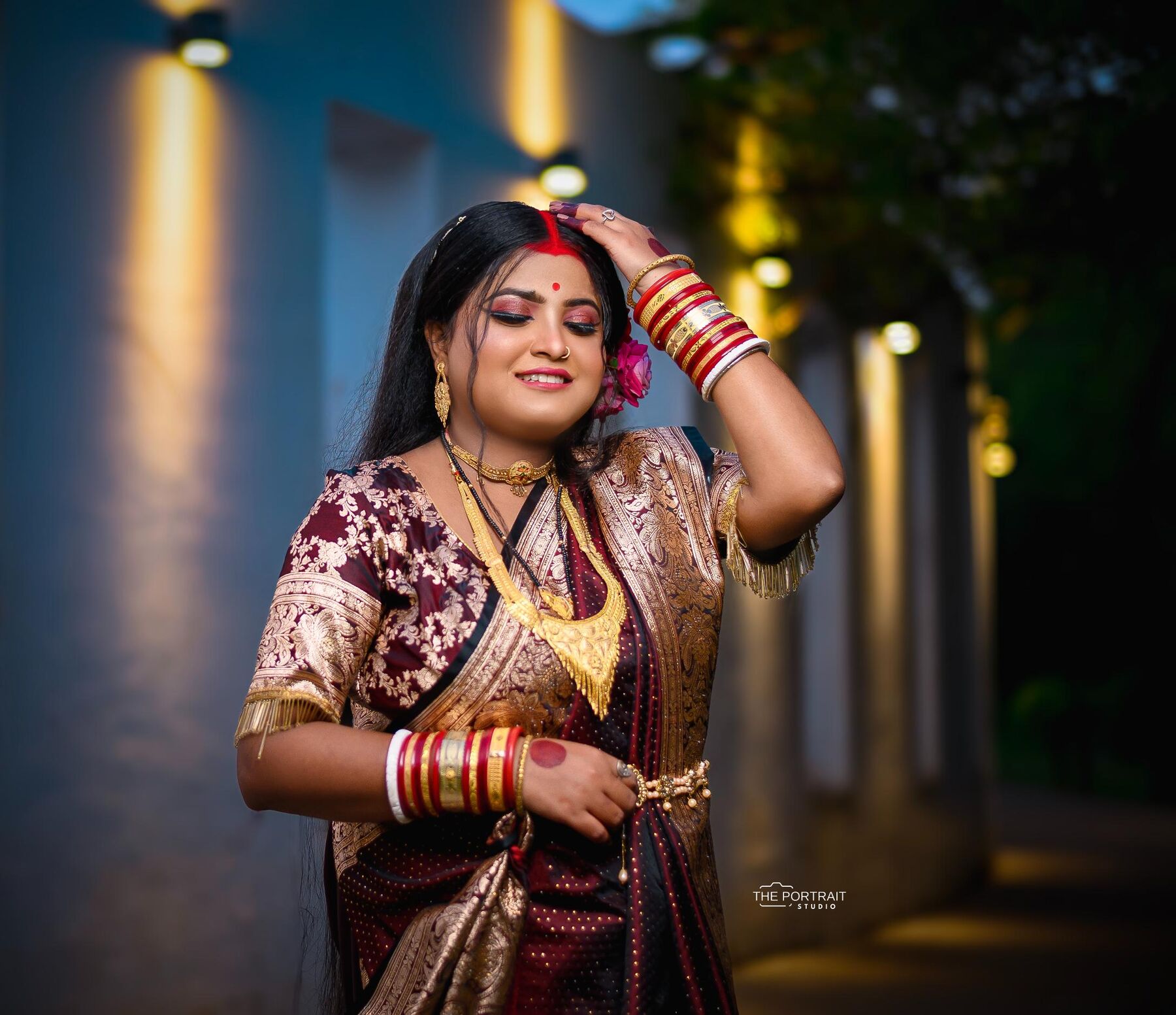 Bride in maroon saree with bangles in a lit corridor